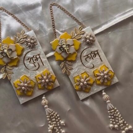Pair of handmade resin Shubh Labh wall hangings with Lord Ganesha, yellow flowers and pearl tassels for home entrance décor.