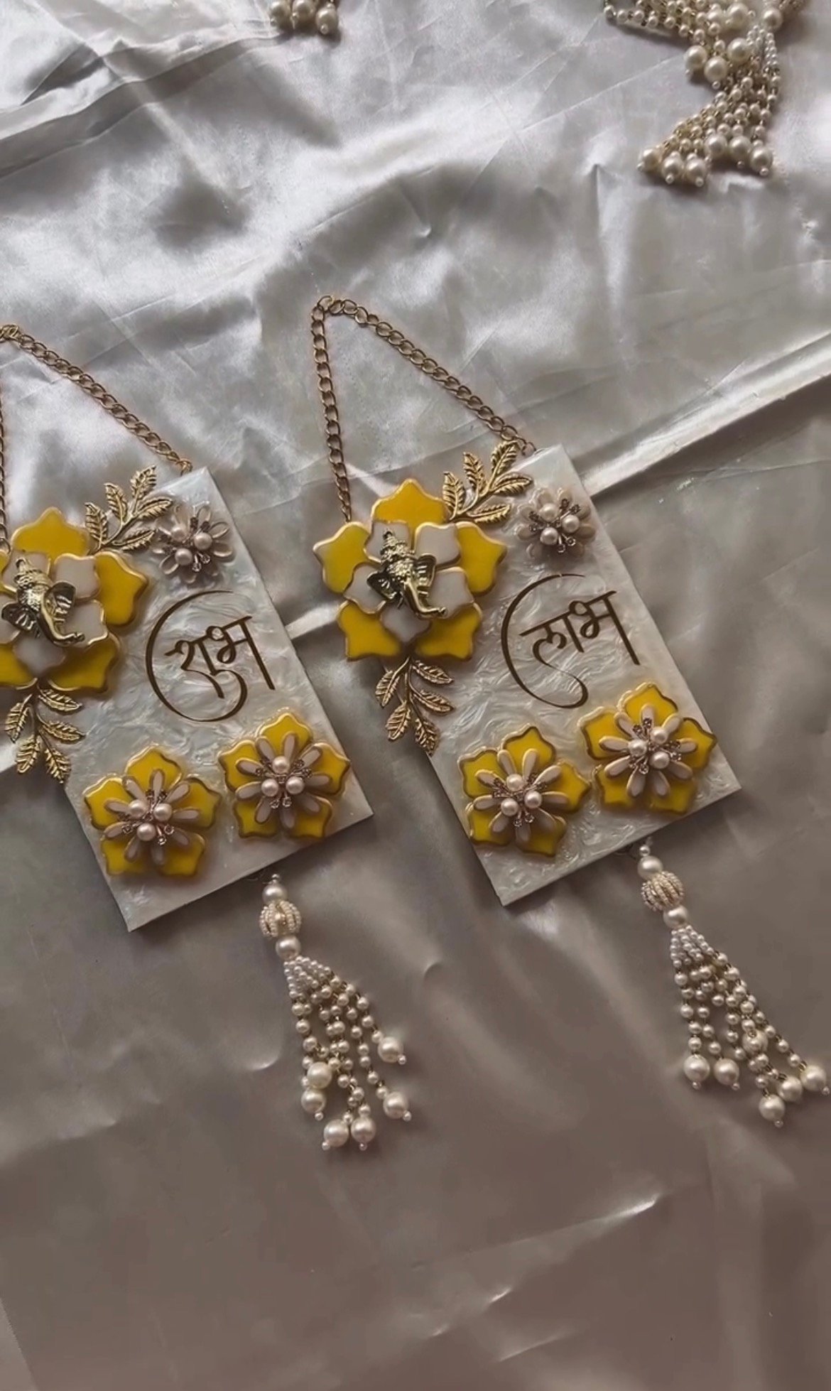 Pair of handmade resin Shubh Labh wall hangings with Lord Ganesha, yellow flowers and pearl tassels for home entrance décor.